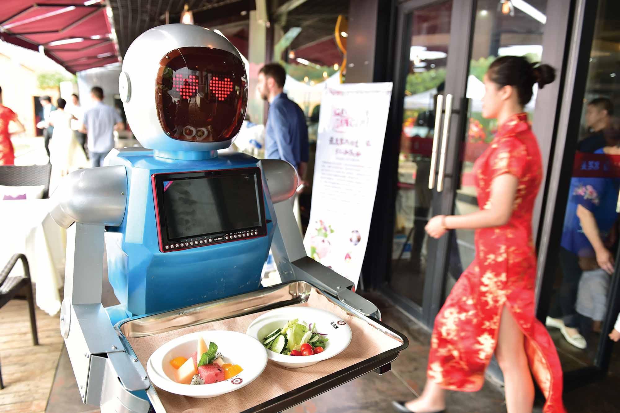 YIWU, CHINA - MAY 18: (CHINA OUT) A "male" robot waiter delivers meals for customers at robot-themed restaurant on May 18, 2015 in Yiwu, Zhejiang province of China. Sophomore Xu Jinjin in 22 years old from Hospitality Management of Yiwu Industrial and Commercial College managed a restaurant where a pair of robot acted as waiters. The "male" one was named "Little Blue" (for in blue color) and the "female" one was "Little Peach" (for in pink) and they could help order meals and then delivered them to customers along the magnetic track and said: "Here're your meals, please enjoy". According to Xu Jinjin, They had contacted with the designer to present more robot waiters to make the restaurant a real one that depends completely on robots. (Photo by ChinaFotoPress/ChinaFotoPress via Getty Images)
